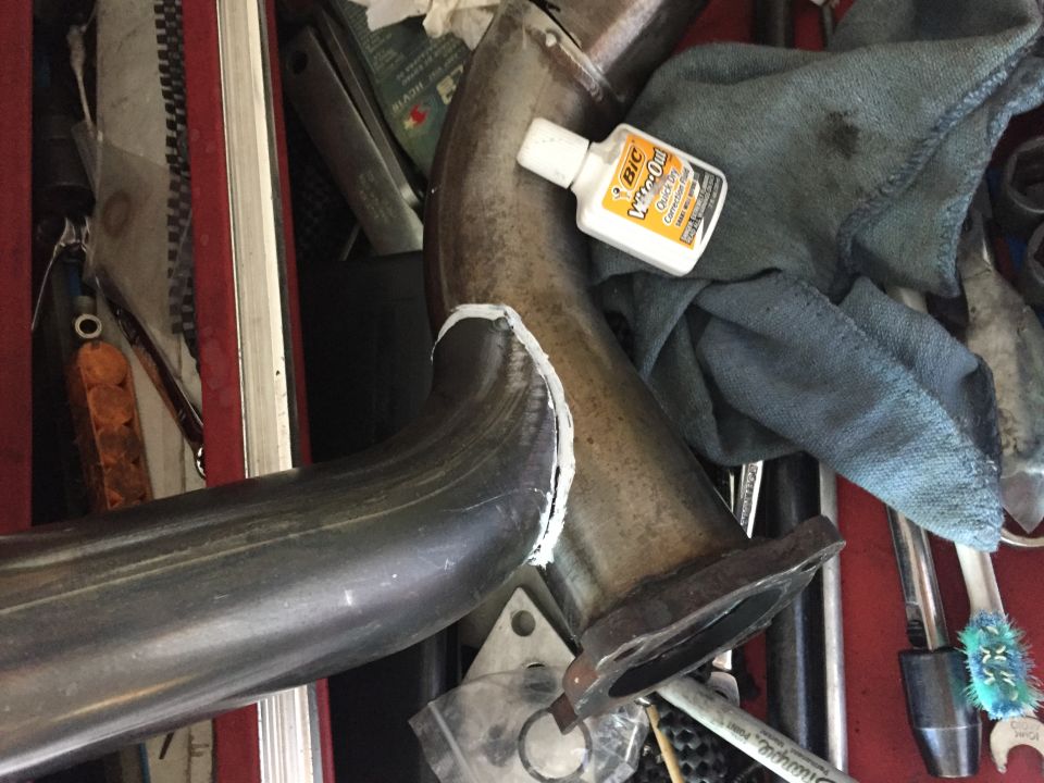 Exhaust pipe section with a bottle of super glue and a rag. Tools are visible in the background