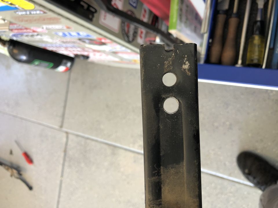 Black slotted steel bracket with two drilled holes held up in a workshop