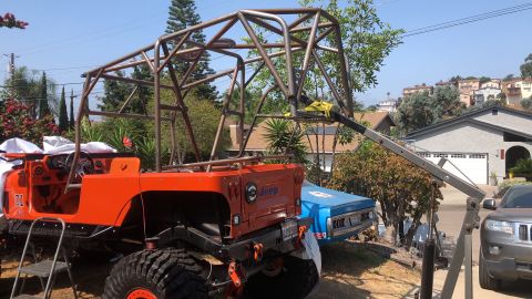 1992 Jeep Wrangler - An orange Jeep is being modified with a custom roll cage, with other vehicles visible in the background.