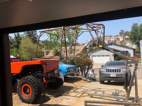 1992 Jeep Wrangler - An orange Jeep CJ-7 is partially visible with a custom roll cage, alongside other vehicles in a driveway.