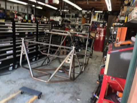 1992 Jeep Wrangler - A bare metal roll cage frame is shown in a workshop setting, surrounded by tool chests and equipment.