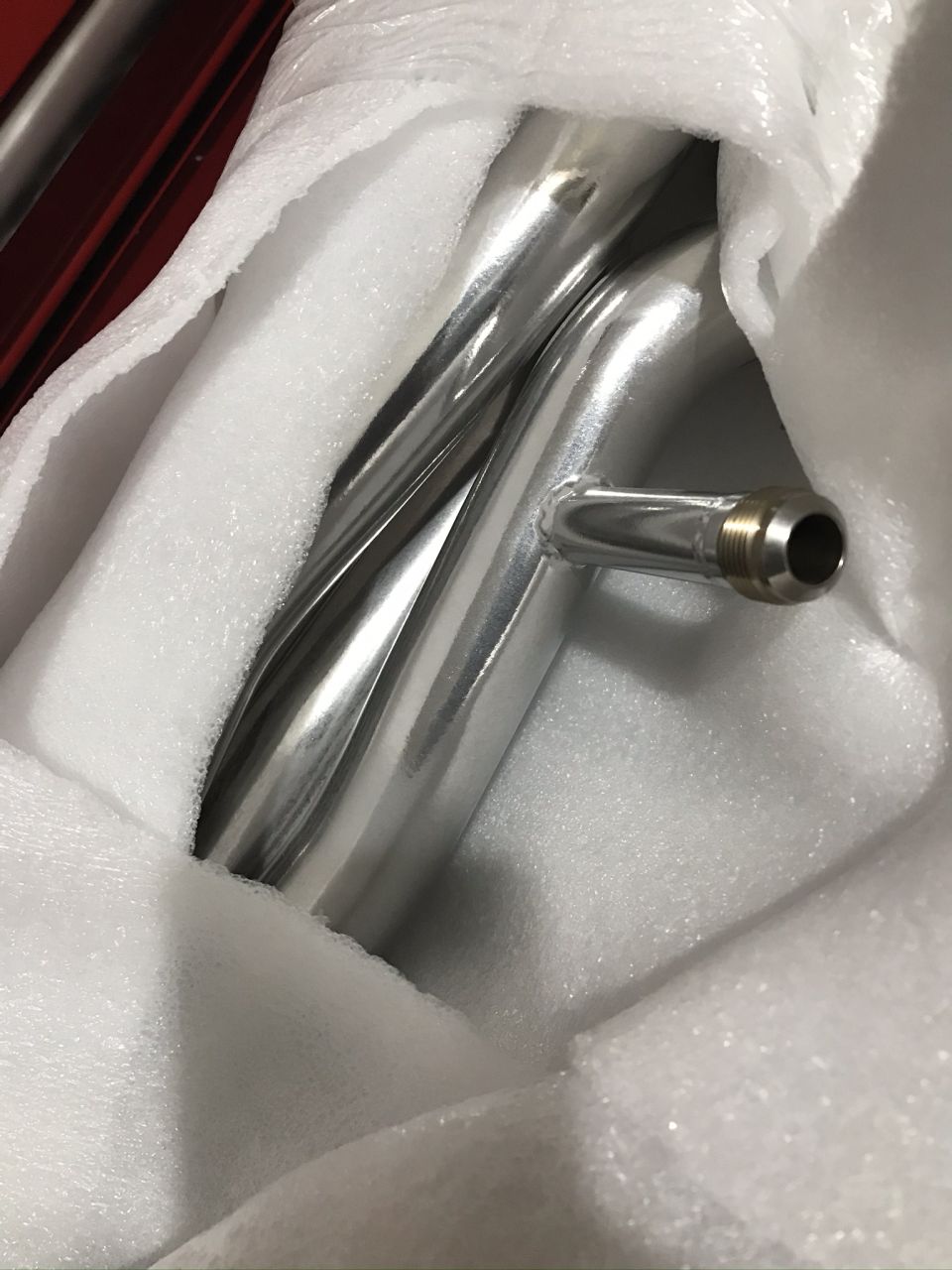 Polished metal pipes with a barbed fitting, wrapped in white foam padding