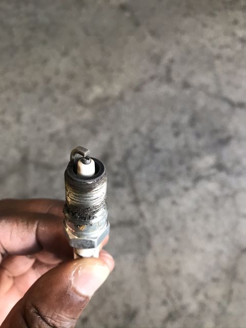 2004 Ford Crown Victoria - A worn spark plug, likely from a vehicle, is held up for inspection against a concrete background.
