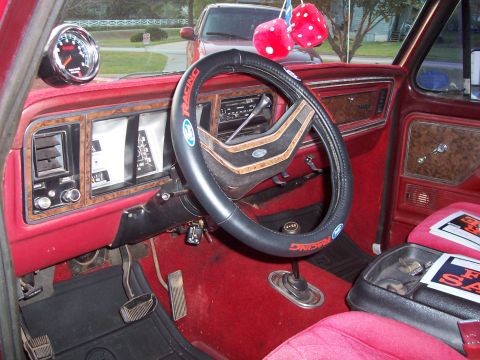 1979 Ford Bronco - The interior of a 1979 Ford Bronco shows a red carpet, wood grain trim, and a tachometer mounted on the dashboard.