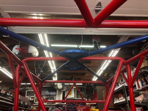 1992 Jeep Wrangler - Custom roll cage structure with red and blue painted tubes, viewed from below in a garage.