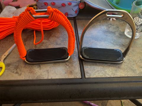 1992 Jeep Wrangler - Horse stirrups, one with orange paracord wrap, sit on a table next to scissors and cord.