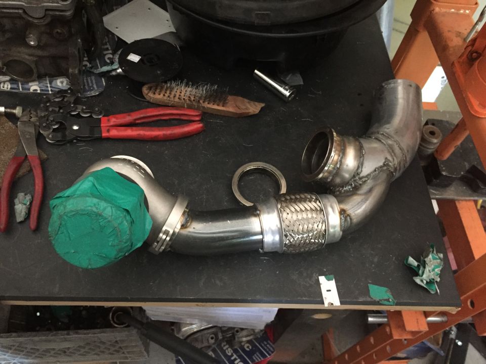 Turbocharger exhaust pipe assembly with red pliers, wire brush, and green tape