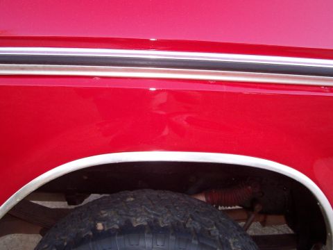1979 Ford Bronco - Close-up of a red vehicle's fender and tire, showing chrome trim and minor dents.