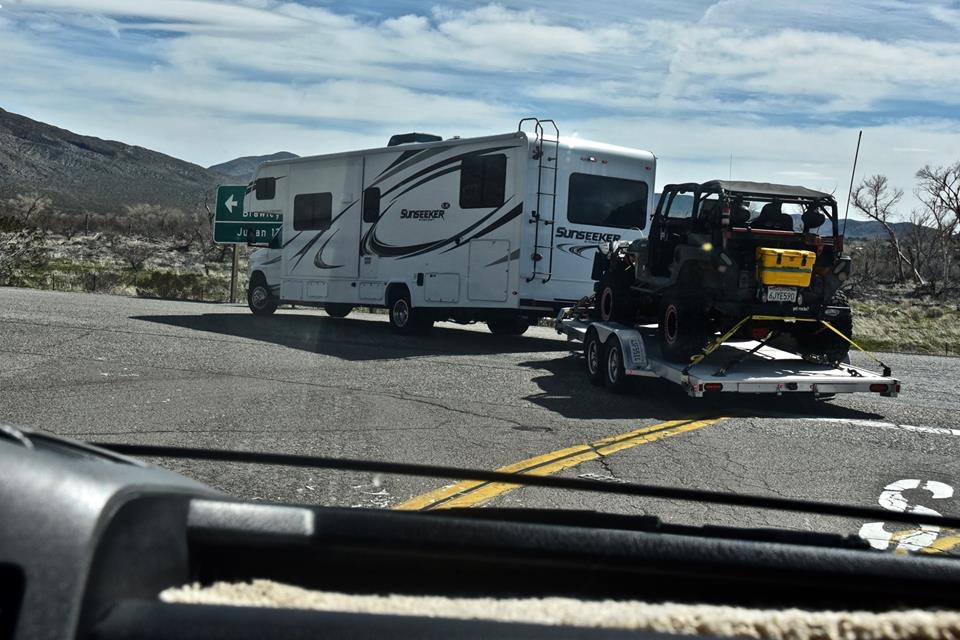 Black Jeep Wrangler on trailer, rear view, with yellow storage box