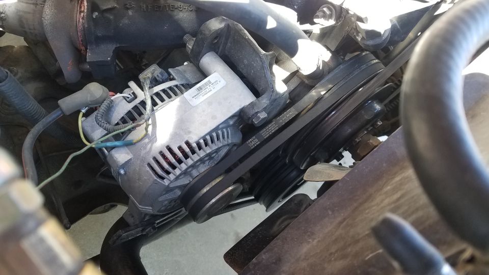 Alternator with a label and drive belts on pulleys in an engine bay