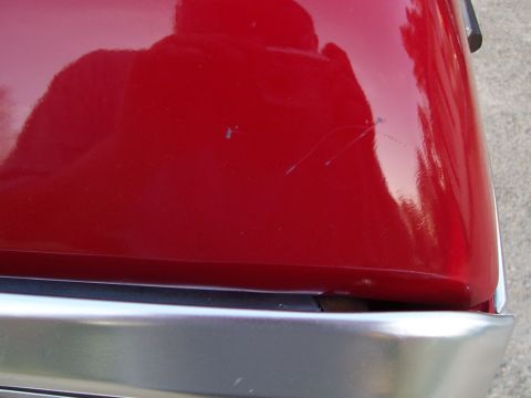 1979 Ford Bronco - Detail of a red car's hood and bumper, showing scratches. Watermark present.