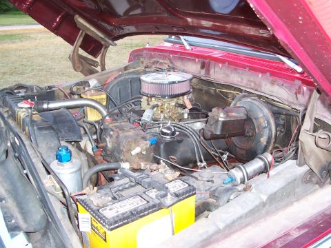1979 Ford Bronco - The engine compartment of a red vehicle is shown with the hood raised, revealing the engine and its components.