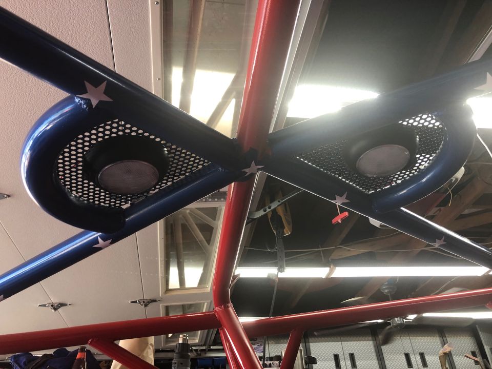 Custom roll cage tubes painted red and blue with white stars. Blue tubes have perforated metal grilles with speakers behind them