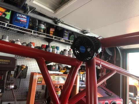 1992 Jeep Wrangler - A red roll cage is the focus, with a small black fan mounted to it. Shelves of supplies are behind.