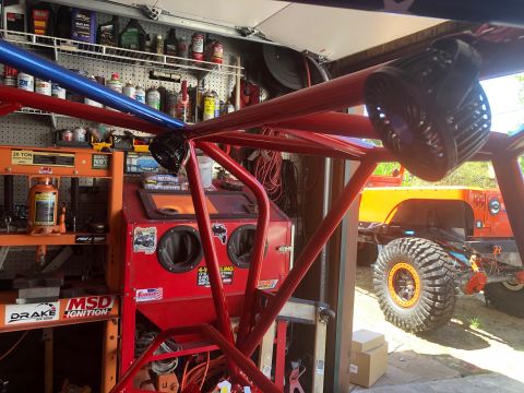1992 Jeep Wrangler - A red roll cage is the primary focus, with an orange Jeep visible behind it in a garage setting.