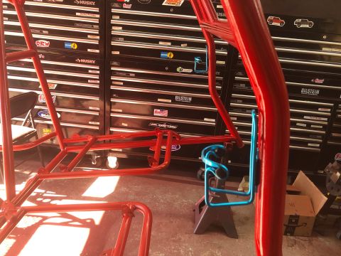 1992 Jeep Wrangler - A red roll cage is shown with a blue cup holder attached, set against a backdrop of tool chests.