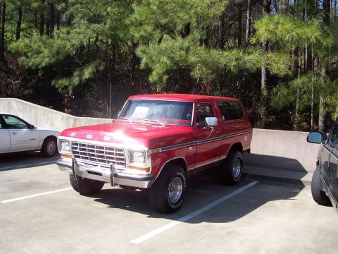1979 Ford Bronco - This red 1979 Ford Bronco is parked in a lot with trees in the background.