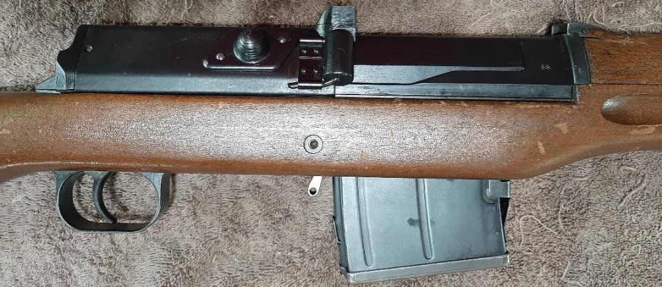 Close-up of a rifle's wooden stock, trigger, and metal magazine