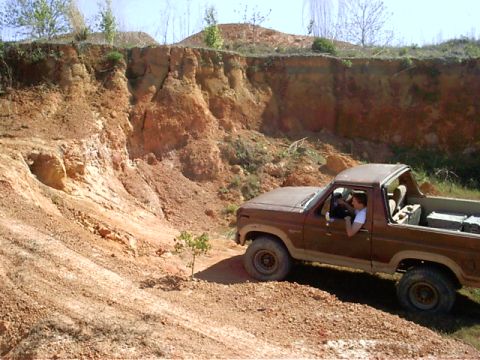 1985 Ford Bronco - A brown Ford Bronco navigates a dirt path next to a steep, eroded cliff face.