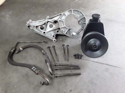1994 Ford Bronco - A collection of power steering components, including a pump, bracket, hoses, and mounting hardware, laid out on a concrete floor.