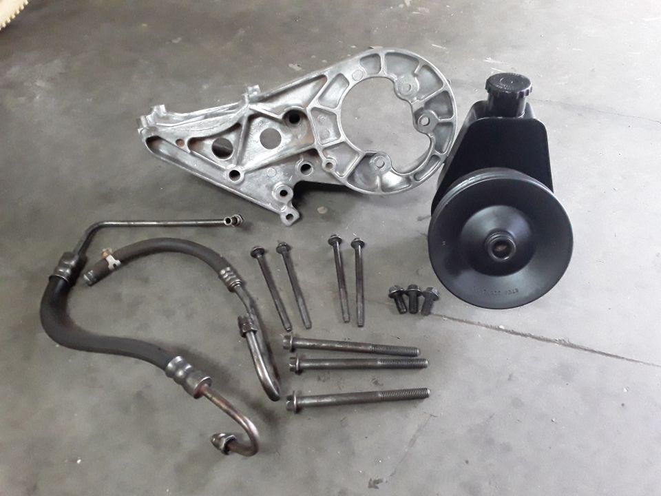Power steering pump, bracket, hoses, and bolts on a gray surface