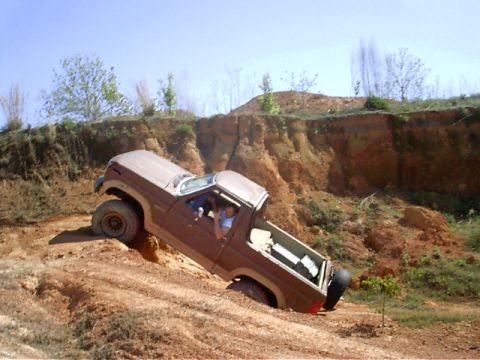 1985 Ford Bronco - A brown 1985 Ford Bronco is stuck in the dirt while off-roading, with two people inside.