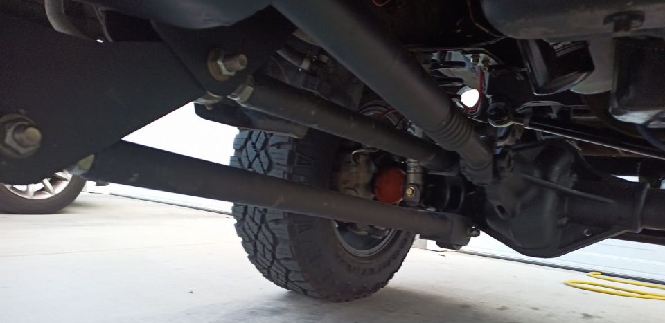 Undercarriage view of a truck's suspension and drivetrain components, including the steering linkage and rear differential