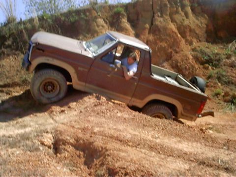 1985 Ford Bronco - A brown Ford Bronco navigates a steep, muddy incline.