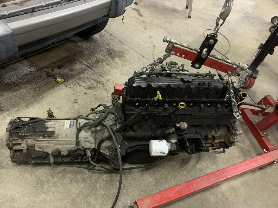 Jeep engine and transmission assembly being worked on, partially attached to an engine hoist