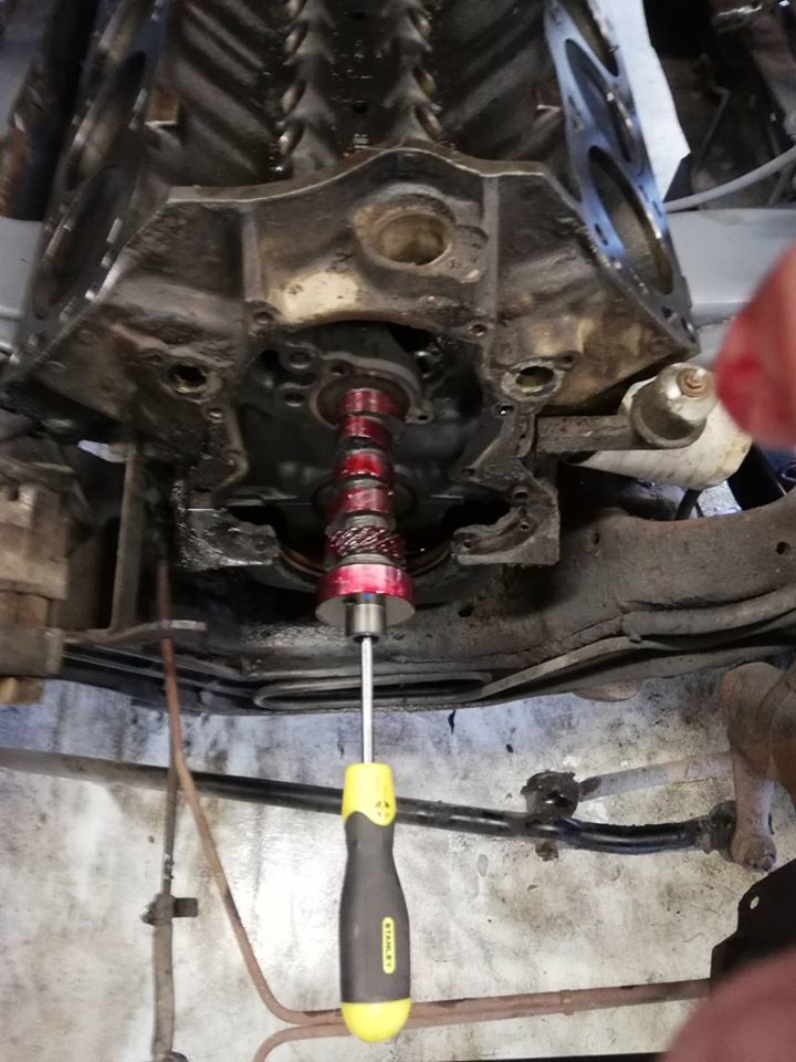 Engine block with red tool inserted into crankshaft pulley area. Yellow-handled screwdriver visible