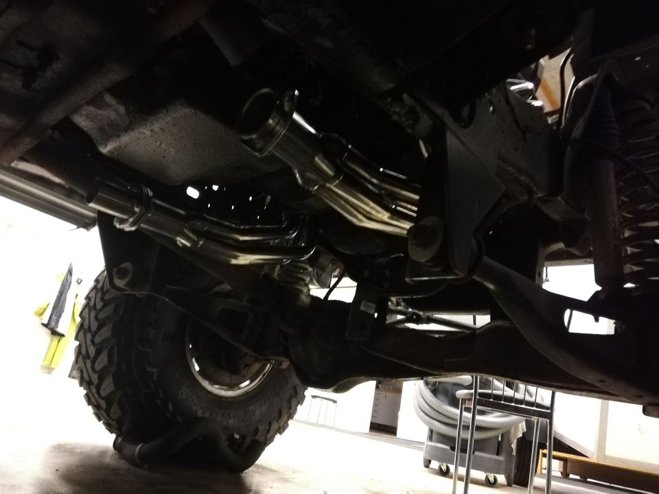 Underside of a vehicle showing a custom exhaust system and large tire