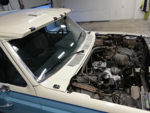 1996 Ford Bronco - The open engine bay of a two-tone white and blue truck reveals its mechanical components and a glimpse of the interior.