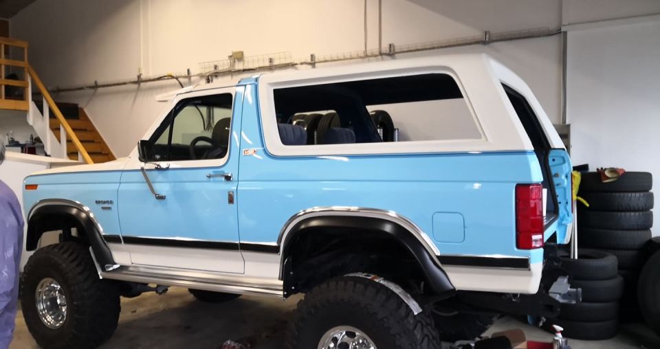 Light blue and white Ford Bronco with white hardtop parked in a shop