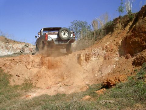1985 Ford Bronco - Ford Bronco navigates a challenging off-road terrain, dust billowing behind it.