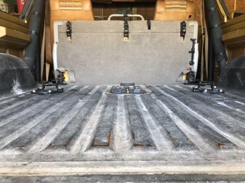 1980 Ford Bronco - Empty ribbed cargo floor of a van or SUV showing seat mounting brackets and a folded gray seat back against the wall.