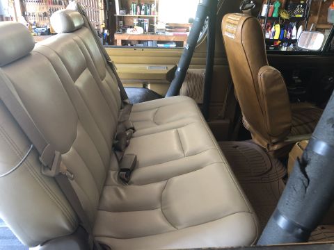 1980 Ford Bronco - The interior of a vehicle shows tan leather seats and seatbelts, with a garage environment visible behind.