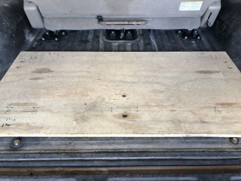 1980 Ford Bronco - The rear interior of a vehicle shows a wooden platform installed over the cargo floor, with a seat base visible above.