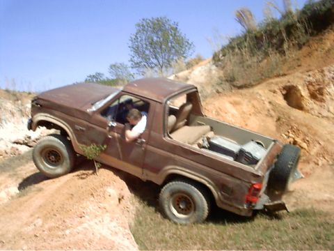 1985 Ford Bronco - A brown SUV navigates a steep, sandy incline under a clear blue sky.