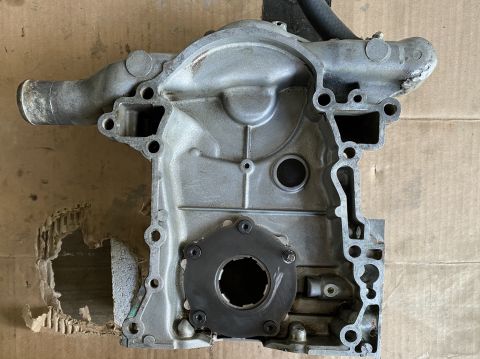 Aluminum engine timing cover with oil pump assembly attached, showing wear and damage to cardboard backing