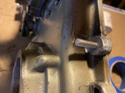 Close-up of a metal engine component with a bolt threaded into it. A coiled spring-like marking is visible on