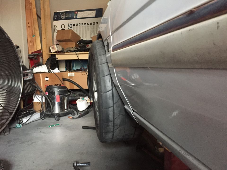 Silver car fender with a wide tire, viewed from the side in a garage