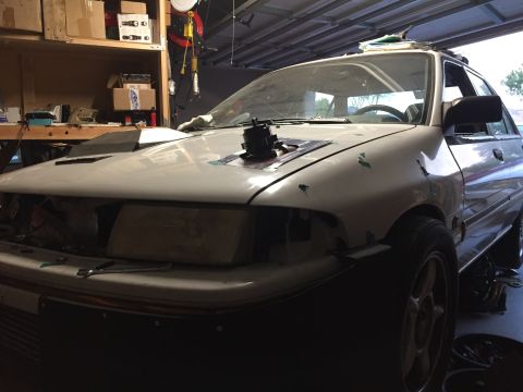 1993 Mercury Tracer - A 1993 Mercury Tracer is seen in a garage with a hood scoop and missing headlight, indicating ongoing modifications.