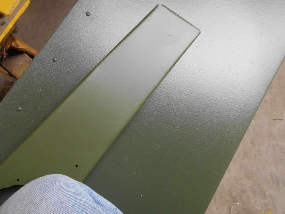 Close-up of two green painted metal panels, one with a raised strip. A person's leg in jeans is visible at the bottom