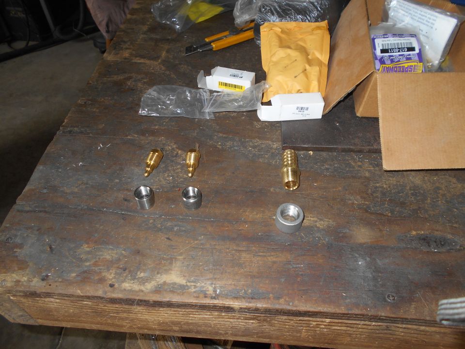 Assortment of brass and silver metal fittings and white boxes on a wooden workbench