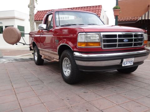 1994 Ford Bronco - This red Ford F-150 pickup truck, likely a 1992 model, is shown from a three-quarter front angle with a spare tire mounted externally on th…