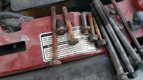 1994 Ford Bronco - A collection of rusty bolts rests on the red hood of a vehicle, obscuring any specific year identification.