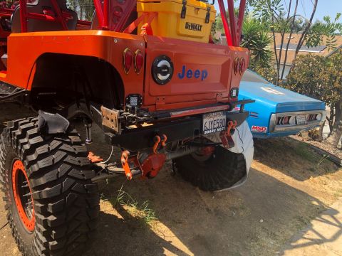 1992 Jeep Wrangler - The rear of an orange 1992 Jeep Wrangler is shown with a blue car parked behind it.