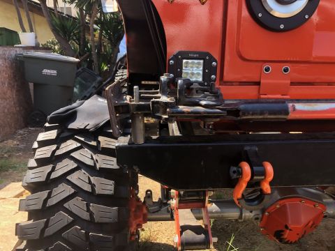 1992 Jeep Wrangler - Close-up of an orange Jeep Wrangler's rear section, a large off-road tire, aftermarket armor, and tow hooks.