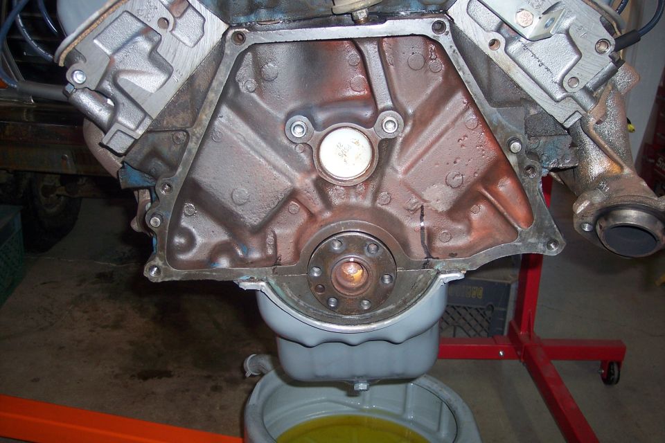 engine block, oil pan, and exhaust manifold on a stand. Oil is draining into a pan