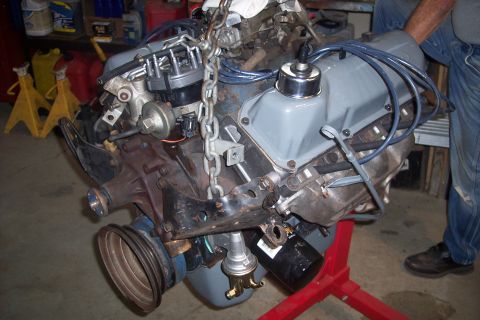 1978 Ford Bronco - Engine assembly suspended by a chain, mounted on a red engine stand.